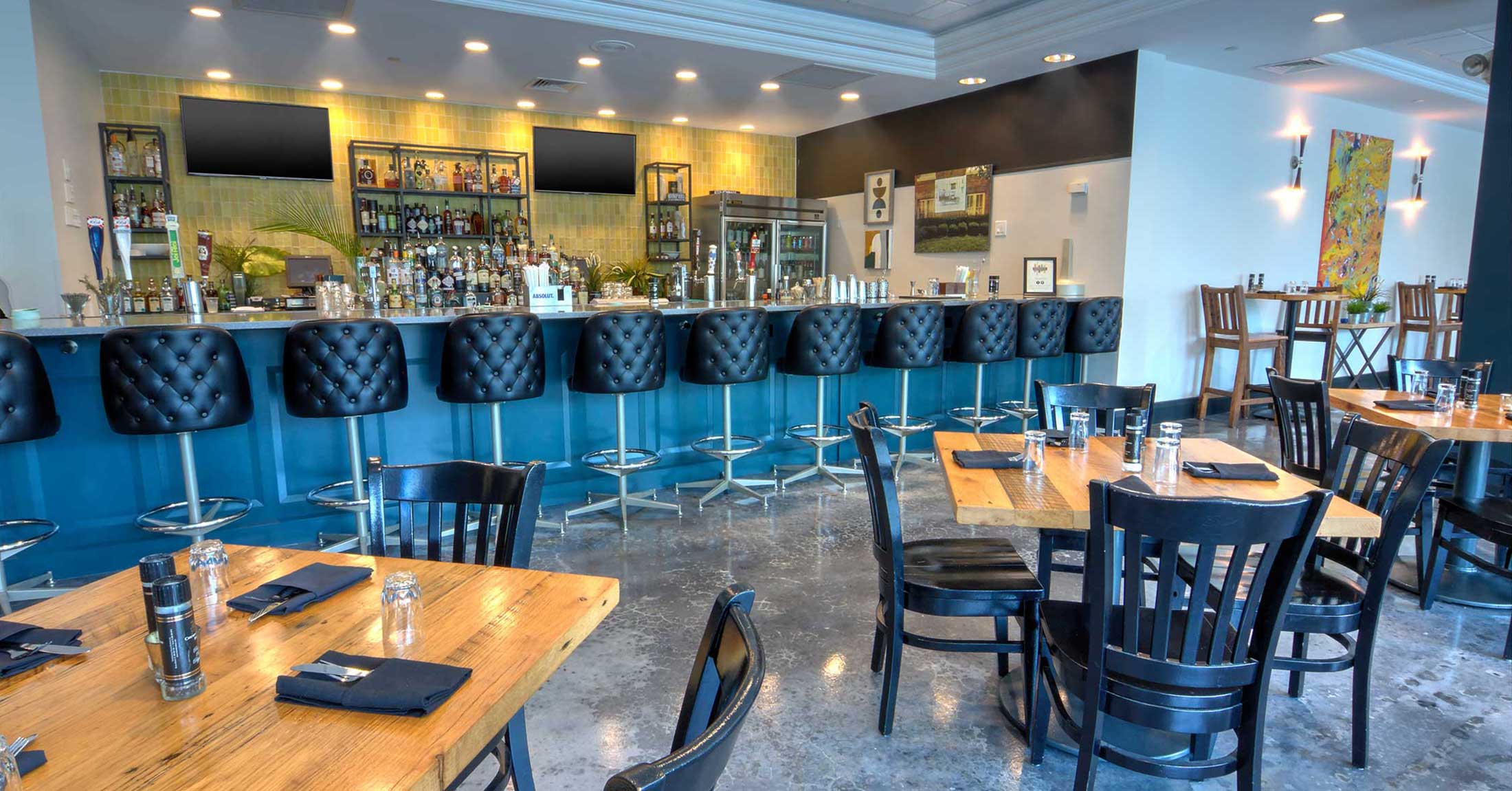 long bar with black bar stools and rustic wooden tables with black chairs in restaurant