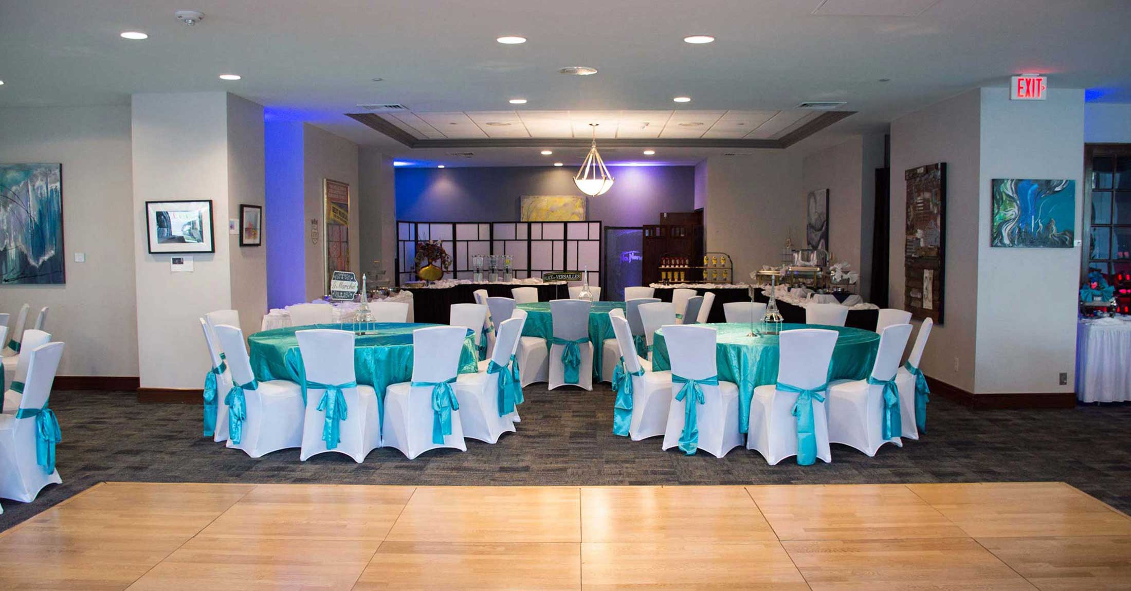 small setup of banquet rounds with with table cloths, white chair covers and teal sashes, dance floor in foreground