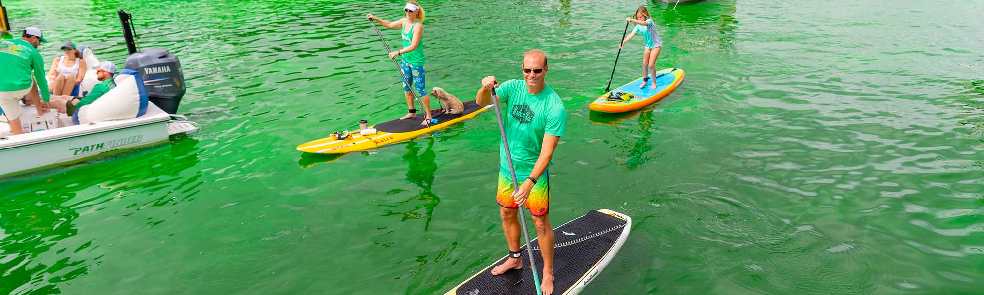 people on stand up paddle boards in the hillsborough river when it was dyed green for st. paddys day