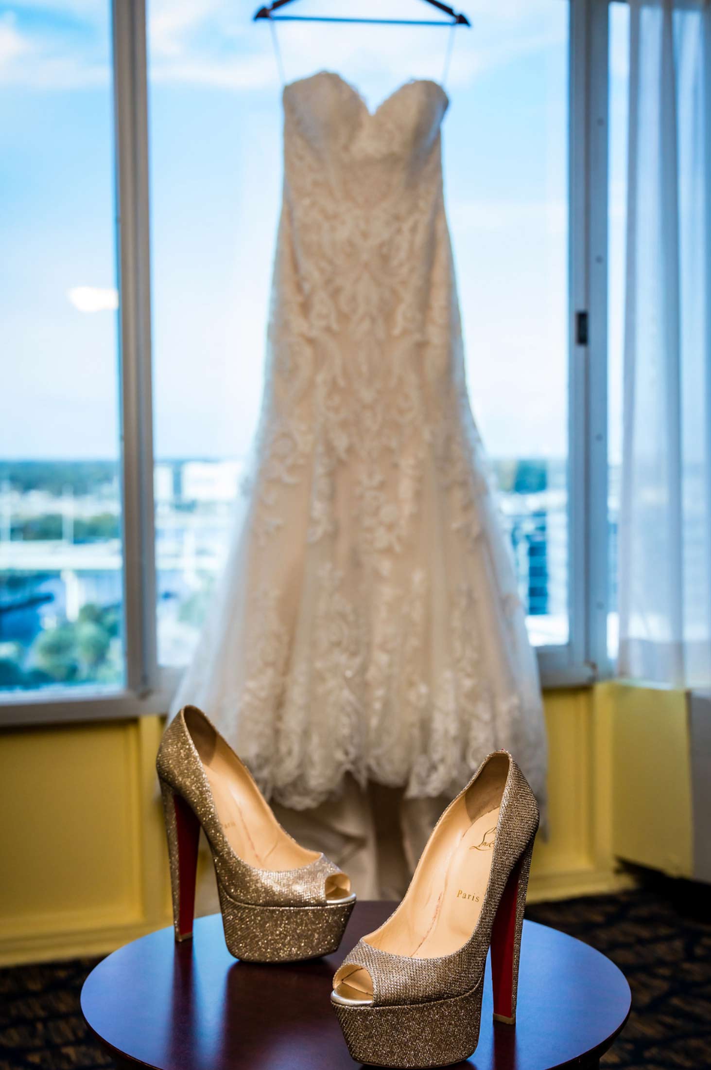 wedding dressing hanging in window and sparkly bridal shoes in foreground on table